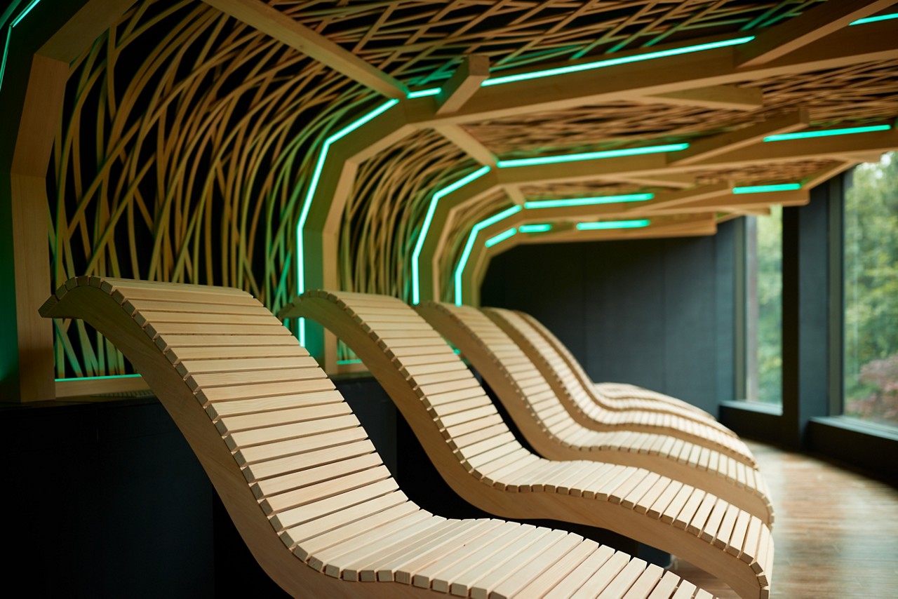 Wooden contoured lounging seats beneath a decorative wooden ceiling design.